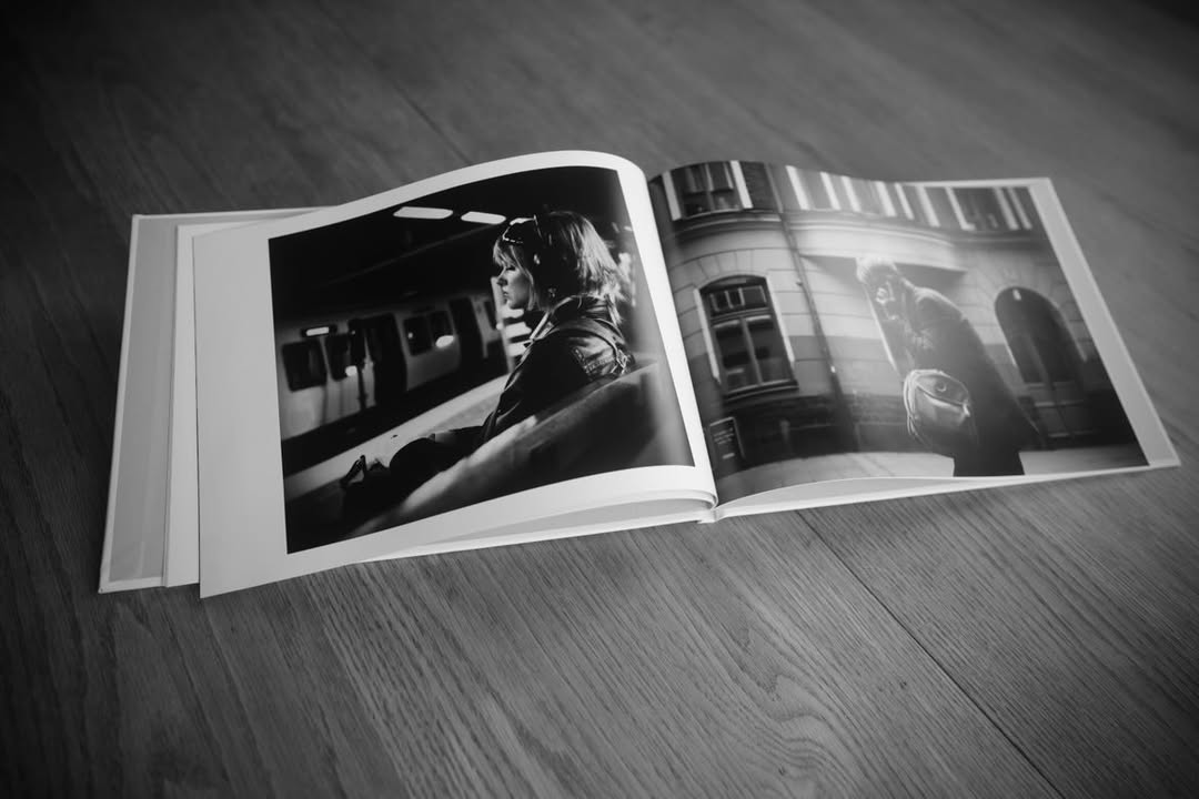 Fotobok lagd uppslagen på ett träbord. SIdorn innehåller varsitt svartvitt fotografi av två människor i stadsmiljö.