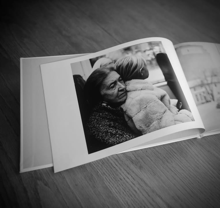 Fotobok från Crimson lagd uppslagen på ett träbord. Ett svartvitt fotografi av en kvinna med ett barn i knät syns på ena sida av uppslaget.