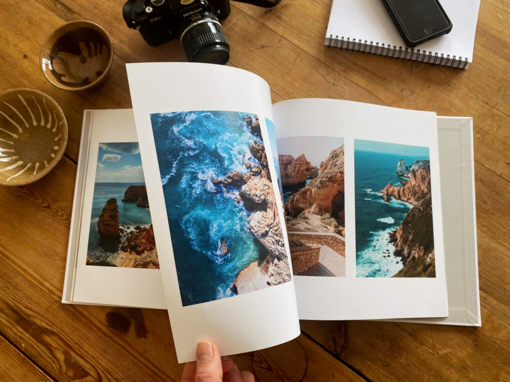 Uppslagen fotobok med bilder av klippor och hav, utlagd på ett träbord